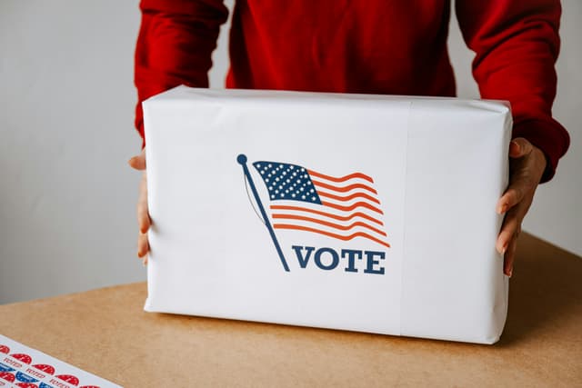 Two hands holding a ballot box with the word Vote on it. 