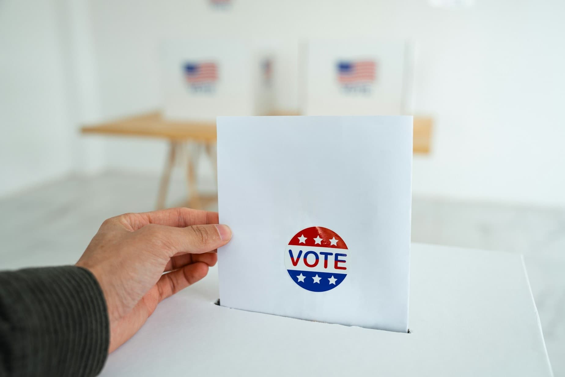 Hand sticking a paper with vote on it in a ballot box.