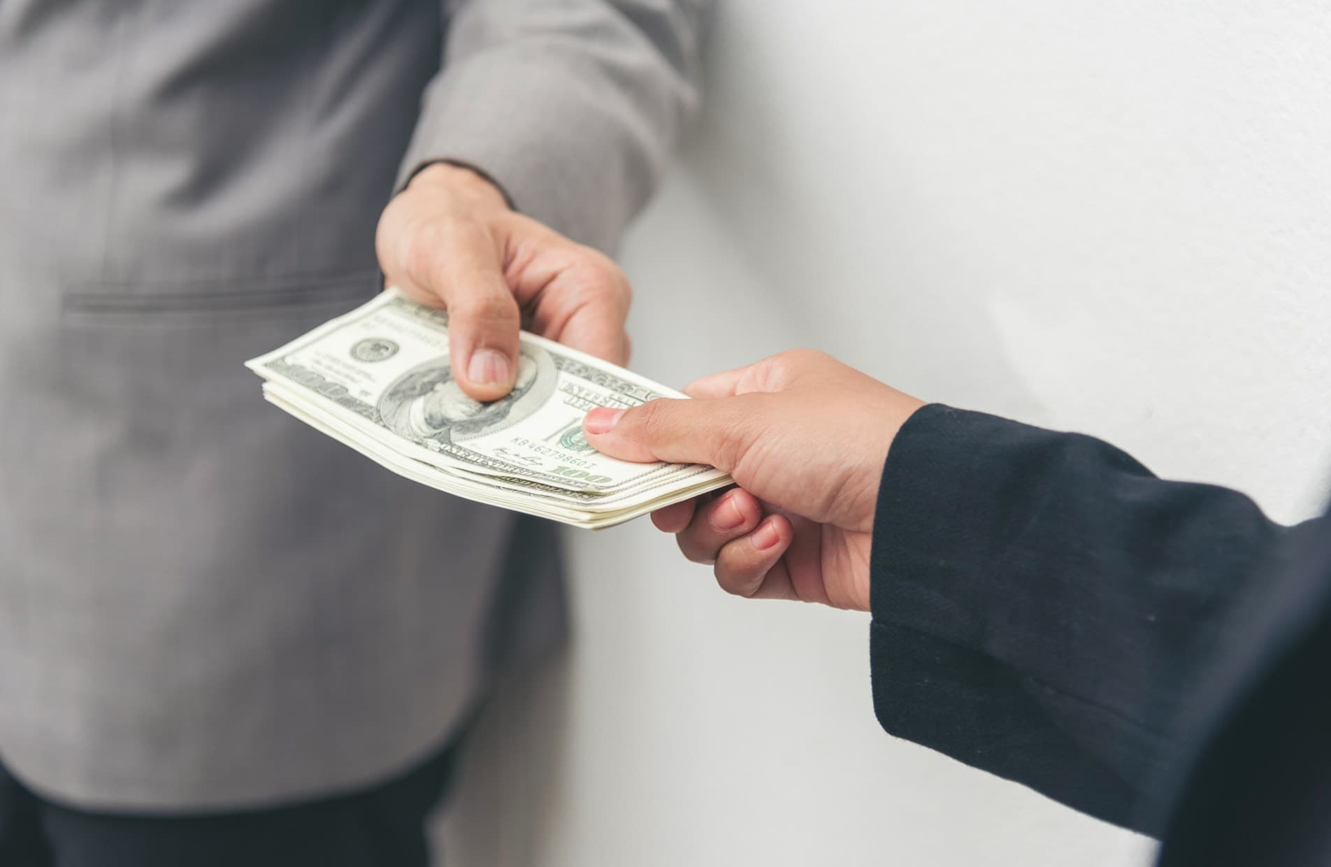 A person in a suit handing another person in a suit money.
