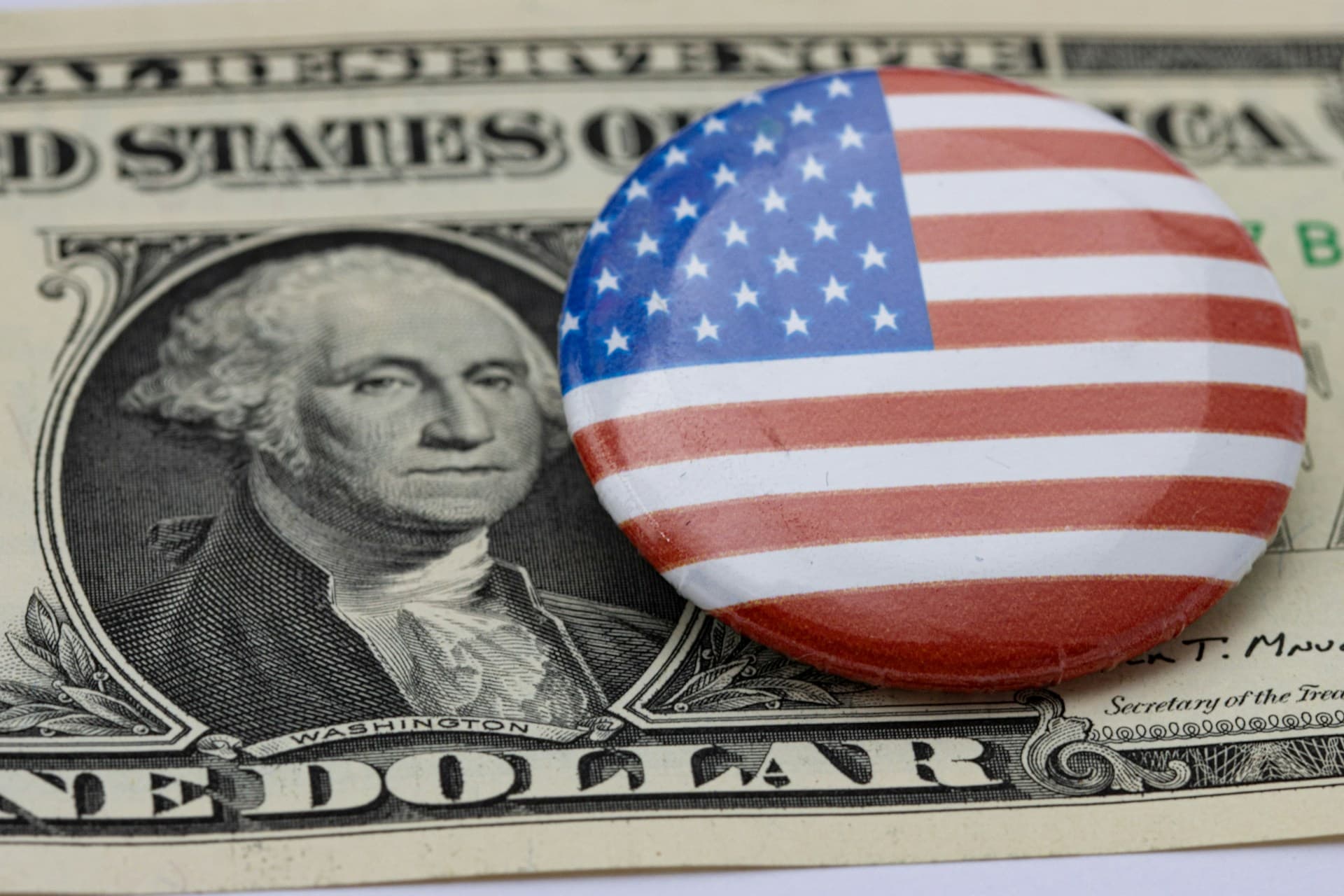 An American flag button on top of a dollar. 