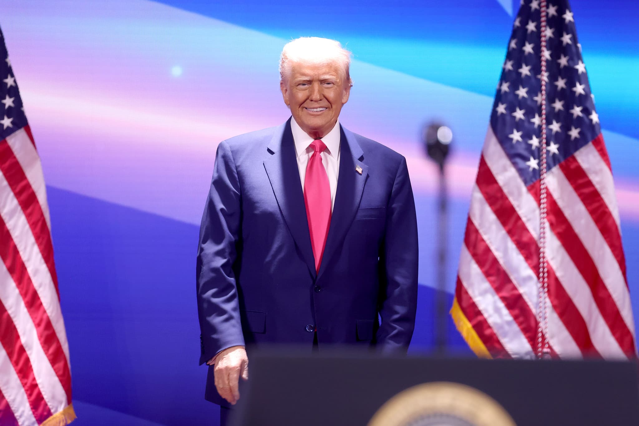 Donald Trump standing behind presidential podium and in front of two American flags.