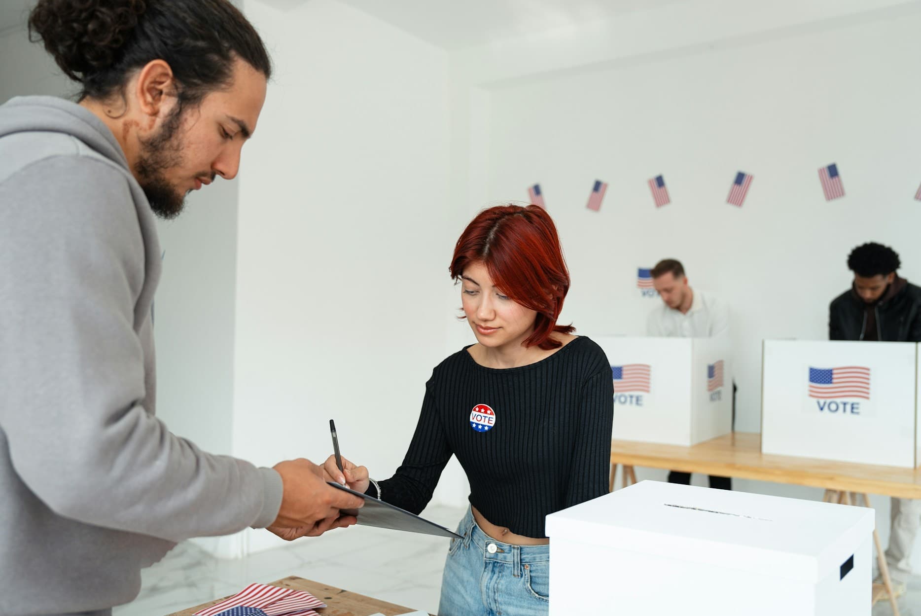 A person filling out a voting form with people voting in the background.