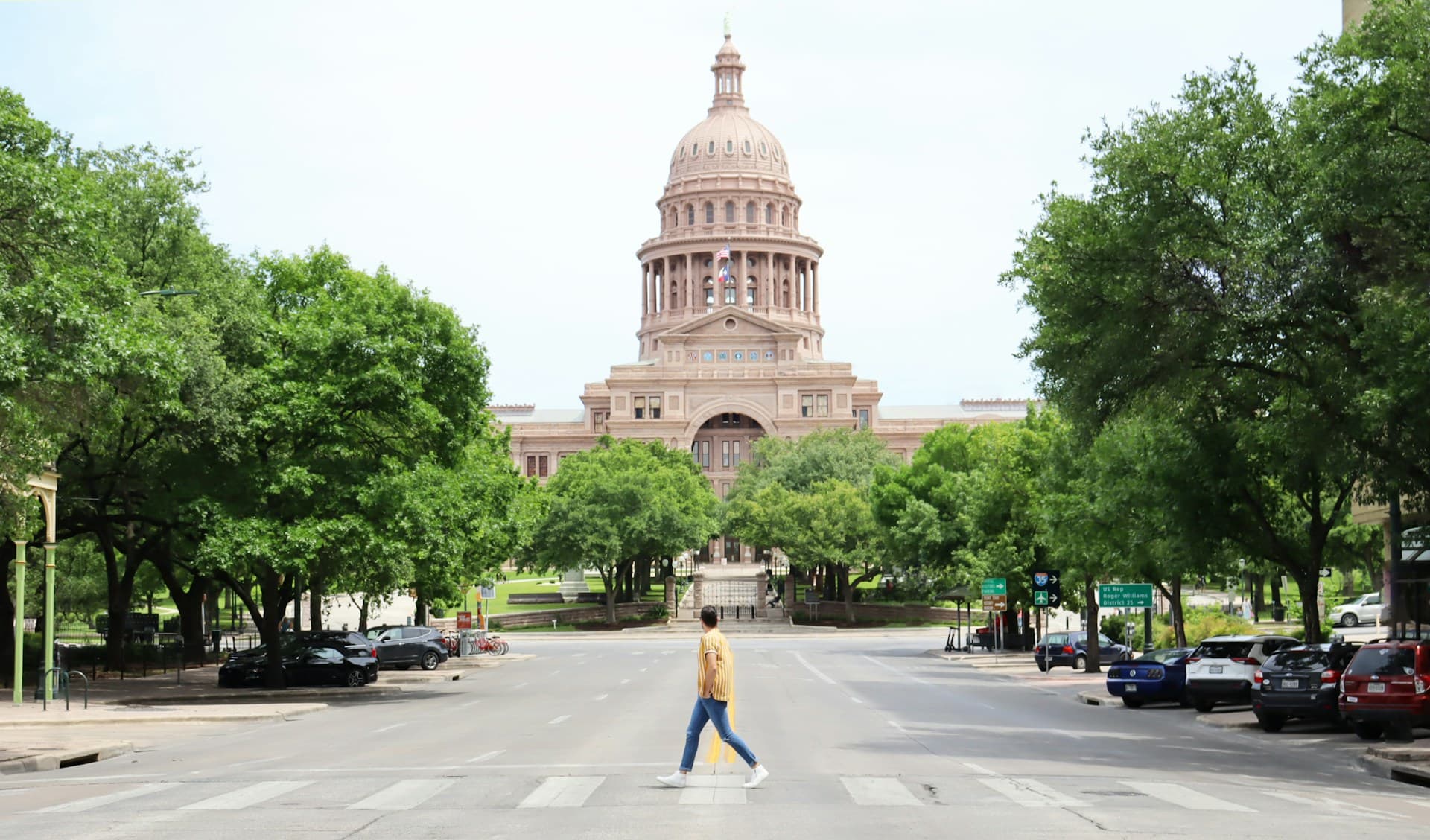 Person walking across the street in front of the Texas Capitol Building.