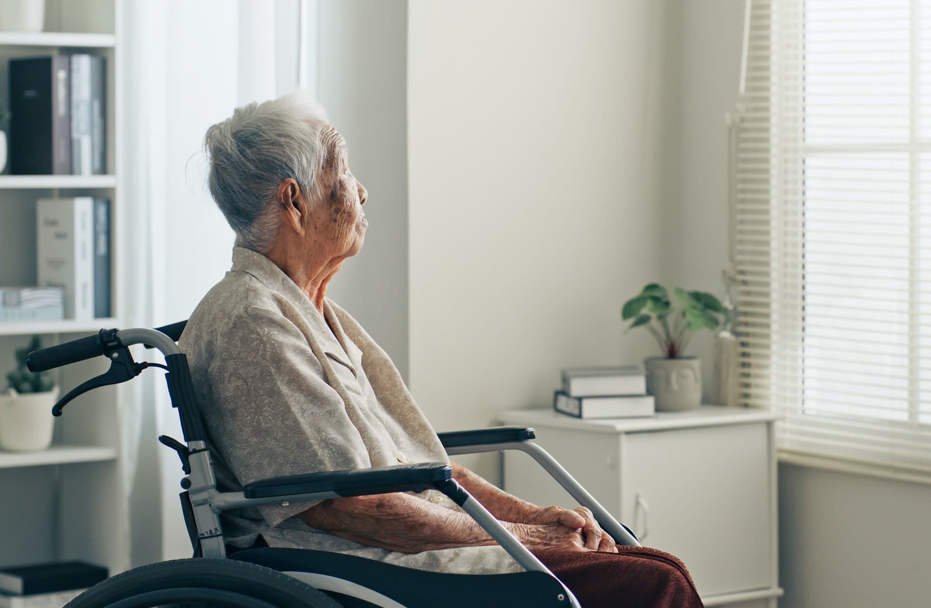 Elderly woman sitting in wheelchair staring out window. 